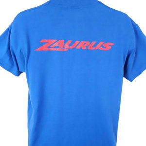 May include: A royal blue t-shirt with a red "ZAURUS" logo printed on the back.