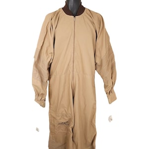 May include: A tan jumpsuit with a zipper closure and a brown collar. The jumpsuit has a pocket on the left leg and a logo on the right leg.