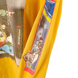 May include: A yellow long-sleeved shirt with a graphic print of a cartoon character and the text "JNCO JEANS USA".