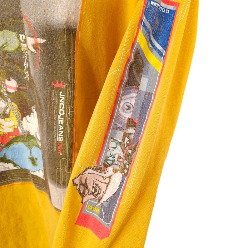 May include: A yellow long-sleeved shirt with a graphic print of a cartoon character and the text "JNCO JEANS USA".