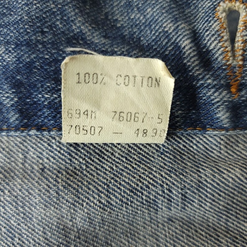 May include: A white tag with the text "100% COTTON" and numbers "6941", "7606", "70507", and "4896" printed on it.