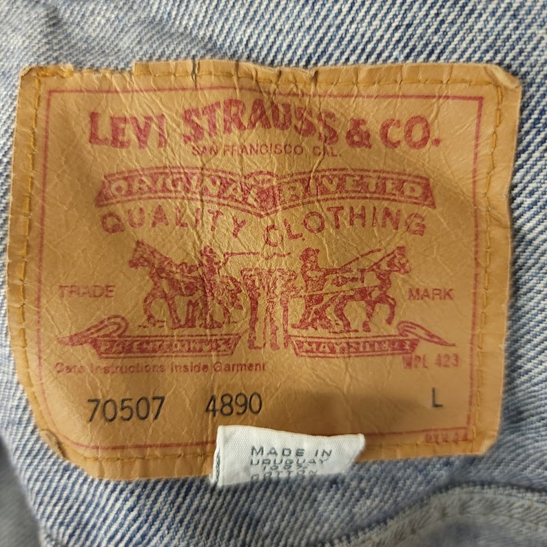 May include: A brown leather Levi Strauss & Co. patch with red stitching. The patch has the company's logo, "Original riveted quality clothing", "Trade Mark", and "Care Instructions Inside Garment". The patch also has the numbers "70507" and "4890" and the letter "L".