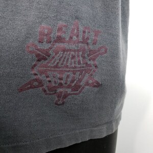 May include: A dark gray t-shirt with a burgundy graphic of a starburst design with the text "REACT BUCKLE BOYS" inside.