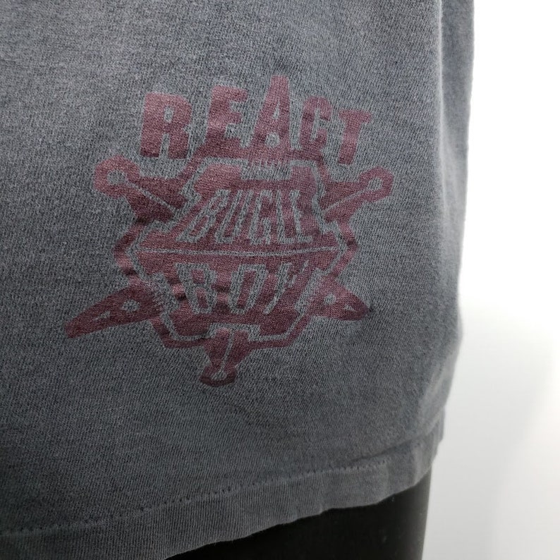 May include: A dark gray t-shirt with a burgundy graphic of a starburst design with the text "REACT BUCKLE BOYS" inside.