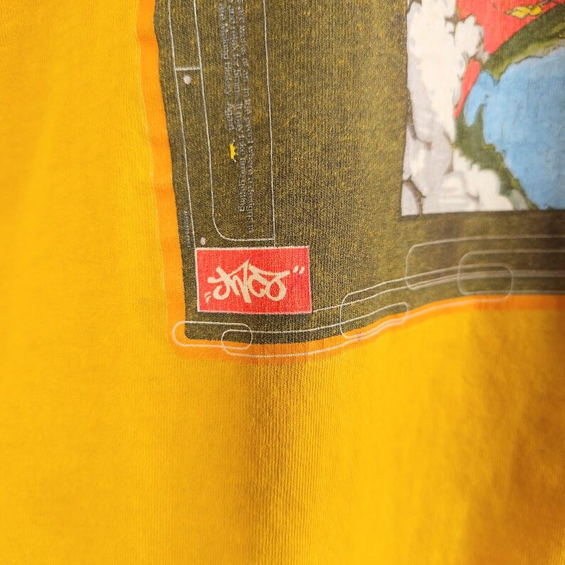 May include: A yellow t-shirt featuring a cartoon character graphic and the word "Shmoo" in a red box.