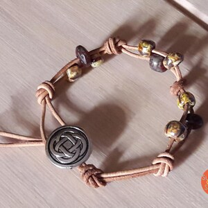 May include: A brown leather bracelet with a silver Celtic knot charm and brown and yellow ceramic beads.