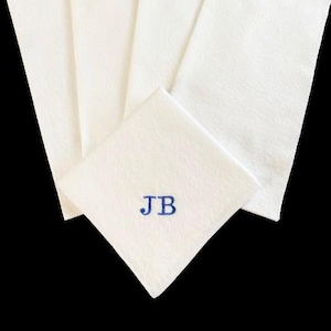 Peut inclure: Plusieurs serviettes blanches en tissu, dont une avec les initiales bleues brodées "JB". Les serviettes sont rectangulaires et présentent une surface texturée. Le fond est noir.