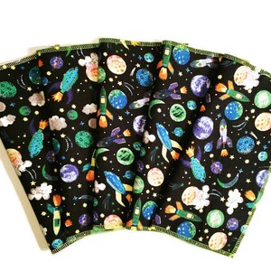 May include: Six black fabric cloths with a colorful space-themed print. The print features planets, rockets, stars, and clouds. The cloths have a yellow border.
