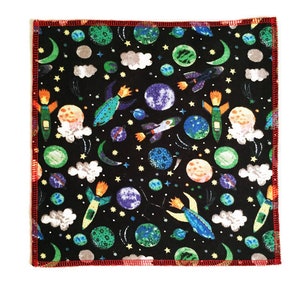 May include: A black fabric square with a red border. The fabric has a repeating pattern of colorful rockets, planets, stars, and clouds.