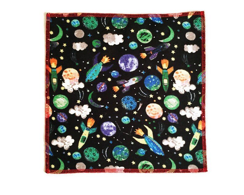 May include: A black fabric square with a red border. The fabric has a repeating pattern of colorful rockets, planets, stars, and clouds.