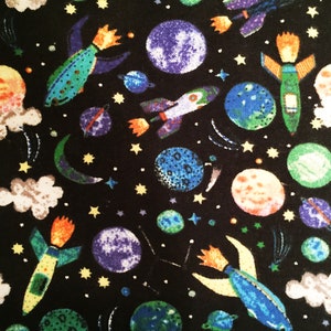 May include: A black fabric with a repeating pattern of colorful rockets, planets, stars, and clouds. The rockets are blue, green, and yellow with orange flames. The planets are blue, green, and orange. The stars are yellow. The clouds are white.