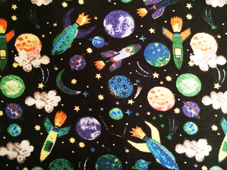 May include: A black fabric with a repeating pattern of colorful rockets, planets, stars, and clouds. The rockets are blue, green, and yellow with orange flames. The planets are blue, green, and orange. The stars are yellow. The clouds are white.