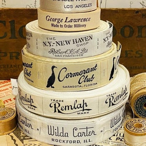 Puede incluir: Una pila de carretes de cinta de tela blanca vintage con texto negro. Los carretes est&aacute;n etiquetados con los nombres de diferentes empresas y ubicaciones, que incluyen "McKiernan's Miracle Mile Los Angeles", "George Lawrence Made to Order Millinery", "The N.Y.-New Haven Shop Robert Kirk, Ltd. San Francisco", "Cormorant Club Sarasota, Florida", "Trade Remlah Mark" y "Wilda Carter Rockford, Ill."