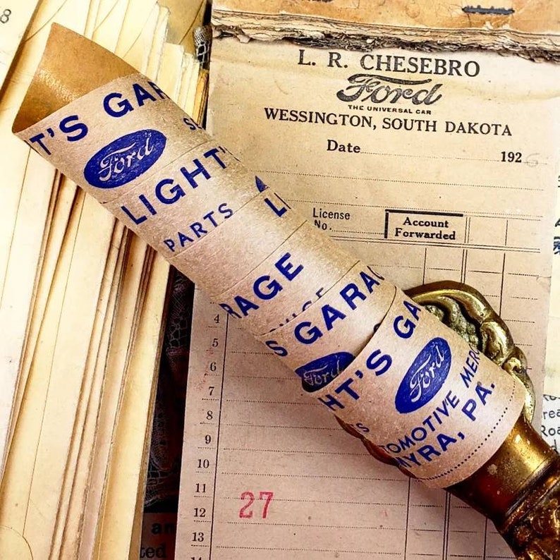 Może przedstawiać: Vintage'owy zw&oacute;j brązowego papieru z niebieskimi i białymi etykietami Forda. Etykiety głosiły "T's Garage", "Ford", "Light Parts", "Garage", "S Garage", "HT's Garage", "Automotive Merchandise" i "Myra, PA".