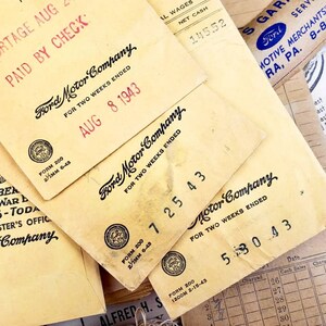 Może przedstawiać: Zbliżenie na kilka zabytkowych czek&oacute;w wypłaty Ford Motor Company z sierpnia 1943 roku. Czeki są zż&oacute;łkłe od czasu i mają logo firmy oraz tekst "Na dwa tygodnie zakończone" wydrukowany na nich.