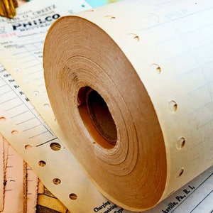 Puede incluir: Primer plano de un rollo de papel perforado, probablemente utilizado en una caja registradora vintage. El papel es beige y tiene un n&uacute;cleo de cart&oacute;n marr&oacute;n. El papel est&aacute; enrollado apretado y tiene una serie de peque&ntilde;os agujeros a lo largo del borde.