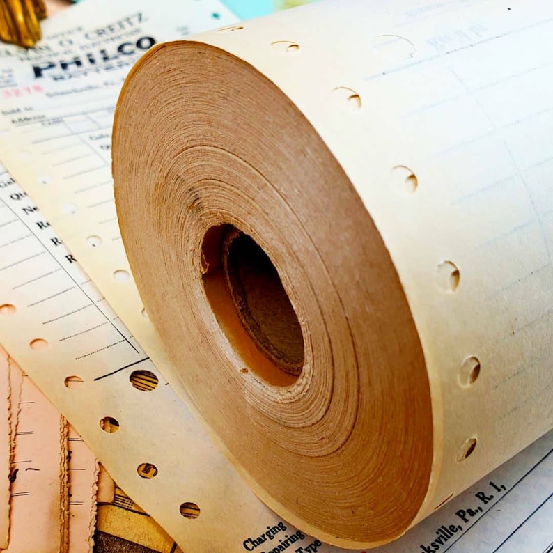 Puede incluir: Primer plano de un rollo de papel perforado, probablemente utilizado en una caja registradora vintage. El papel es beige y tiene un n&uacute;cleo de cart&oacute;n marr&oacute;n. El papel est&aacute; enrollado apretado y tiene una serie de peque&ntilde;os agujeros a lo largo del borde.