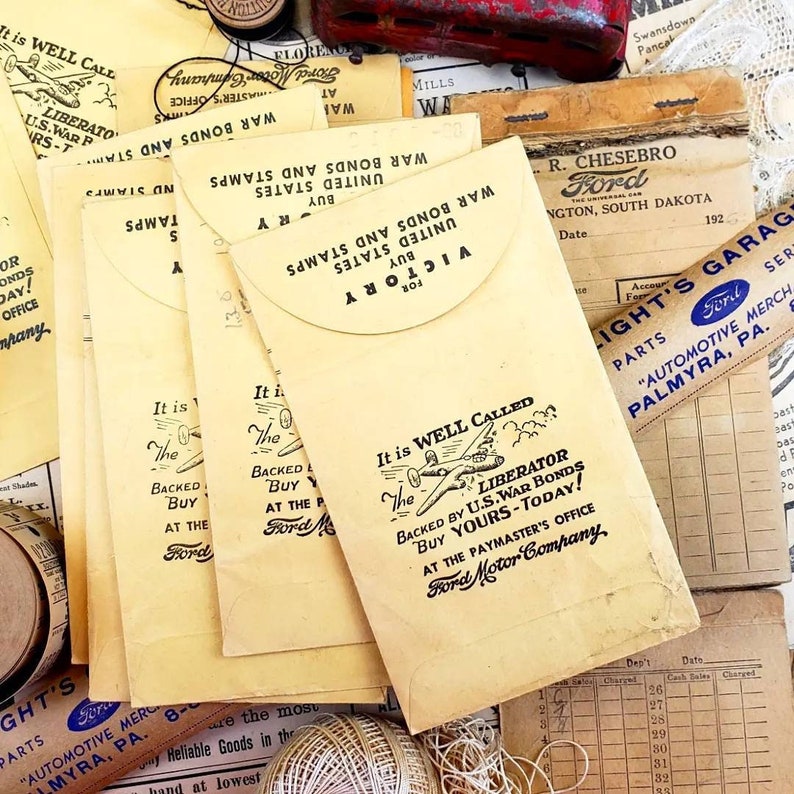 Może przedstawiać: Stos vintage'owych kopert z ż&oacute;łtym tłem i czarnym tekstem. Koperty służą do kupowania amerykańskich obligacji wojennych i zawierają tekst "It is well called the Liberator" i "Backed by U.S. War Bonds Buy Yours Today!" Koperty pochodzą z Ford Motor Company.