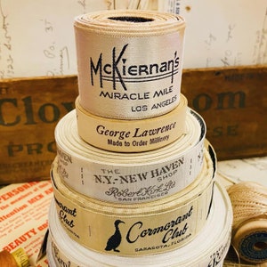 Puede incluir: Una pila de carretes de cinta vintage con etiquetas. El carrete superior tiene una etiqueta que dice "McKiernan's Miracle Mile Los Angeles". El siguiente carrete hacia abajo tiene una etiqueta que dice "George Lawrence Made to Order Millinery". El tercer carrete hacia abajo tiene una etiqueta que dice "The NY-New Haven Shop Robert Kirk, Ltd. San Francisco". El carrete inferior tiene una etiqueta que dice "Cormorant Club Sarasota, Florida".