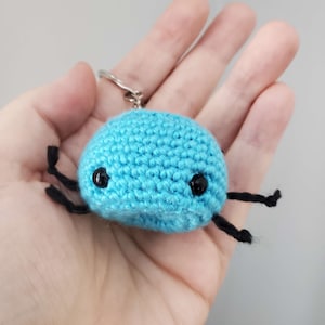 May include: A blue crocheted keychain with black yarn legs and black button eyes.
