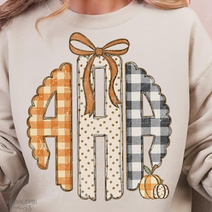 May include: A beige crewneck sweatshirt featuring a large central graphic of three letters arranged in a monogram style. The left letter has an orange gingham pattern, the center has tan polka dots, and the right has a black and white buffalo check.