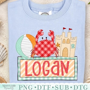 May include: Light blue t-shirt featuring a beach-themed graphic. The design includes a red gingham crab, a beach ball, a sandcastle, and the name "LOGAN" in red letters on a striped background. The shirt is perfect for summer.