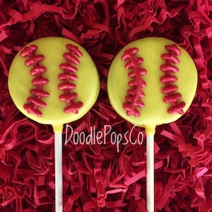 May include: Two yellow and red softball cake pops on white sticks. The cake pops are decorated to look like softballs with red stitching.