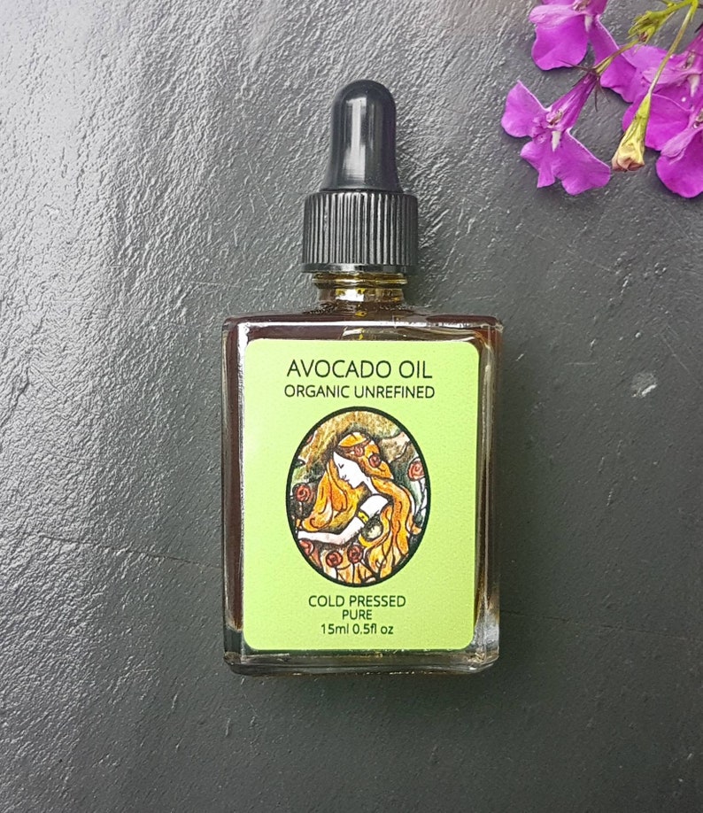 May include: A glass bottle of organic, cold-pressed avocado oil. The label is green and features a drawing of a woman with long hair. The label reads "Avocado Oil Organic Unrefined Cold Pressed Pure 15ml 0.5fl oz."