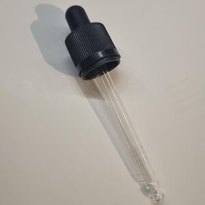 May include: A clear glass dropper with a black plastic cap. The dropper has a long, thin tube and a bulb at the end.