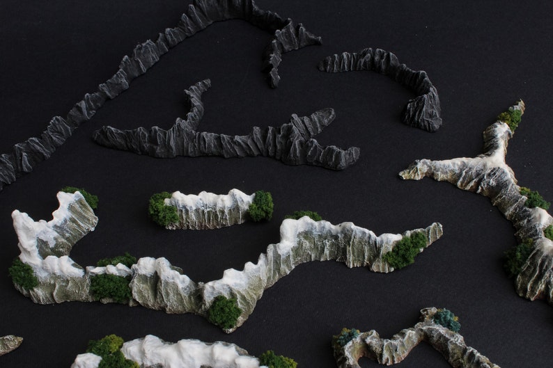 May include: A set of five miniature mountain ranges made of gray and white painted foam. The mountains are arranged in a curved pattern on a black background.