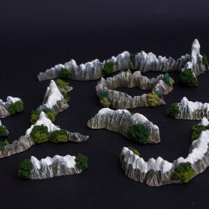 May include: A set of miniature mountain terrain pieces for tabletop gaming. The pieces are made of a light gray material with green accents and are designed to resemble snow-capped mountains.
