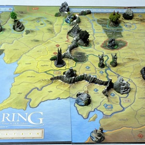 May include: A game board depicting a map of Middle-earth with miniature figures representing various locations and characters from the Lord of the Rings universe. The board game is called "Warring" and features a second edition.