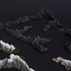 May include: A set of miniature mountain ranges made of gray and white textured material. The mountains are arranged in a circular pattern on a black surface.