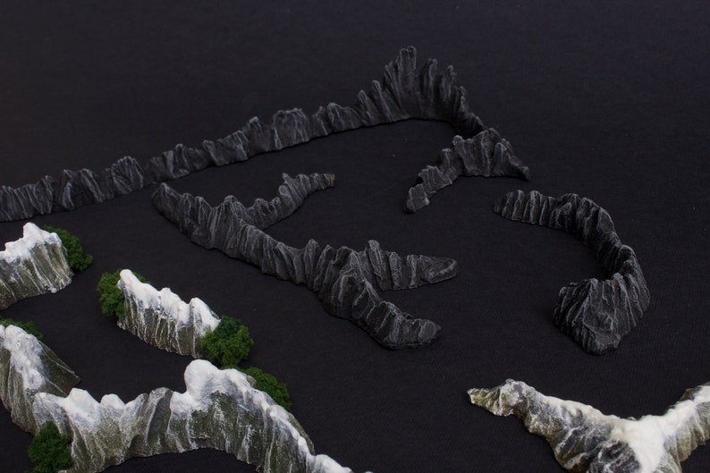 May include: A set of miniature mountain ranges made of gray and white textured material. The mountains are arranged in a circular pattern on a black surface.