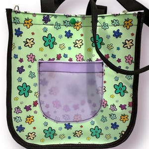 May include: A green tote bag with a floral print and a clear zippered pocket. The bag has black straps and a black trim.