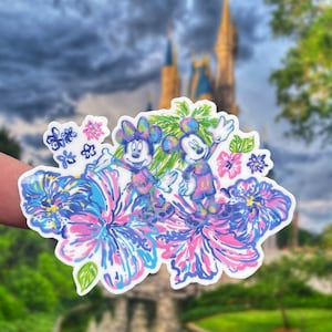 以下が含まれることがあります： ピンク、ブルー、グリーンの花が咲く熱帯の風景にミッキーマウスとミニーマウスが描かれたステッカー。ステッカーは白で光沢のある仕上げです。