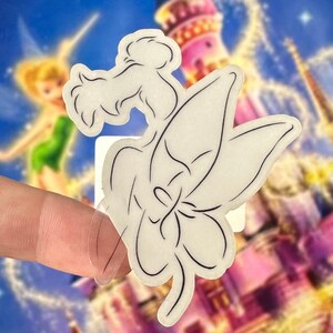 May include: A white vinyl sticker with a black outline of a fairy sitting on a flower. The sticker is clear and has a glossy finish.