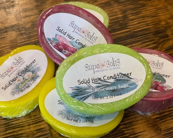 May include: Five oval-shaped solid hair conditioner bars in various colors. The bars are labeled with the brand name "Sapo Solis" and the scent of each bar. The scents are: Chamomile, Strawberry, Rosemary Sage, and Lava.