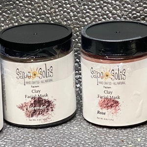 May include: Four glass jars of clay facial masks with black lids. The jars are labeled with the brand name "Sapo Solis" and the scent of each mask: Activated Charcoal, Lavender, Rose, and Turmeric.