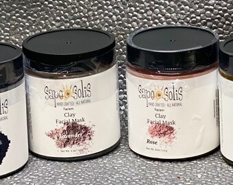 May include: Four glass jars of clay facial masks with black lids. The jars are labeled with the brand name "Sapo Solis" and the scent of each mask: Activated Charcoal, Lavender, Rose, and Turmeric.