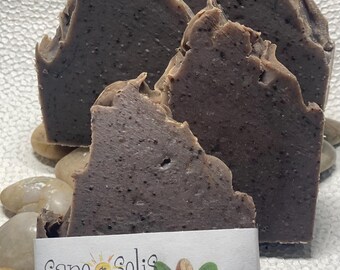 May include: Three bars of dark brown African Black Soap, hand-crafted and all-natural, with a label that reads "Sapo de Solis" and "Net Wt 4-5 oz / 118 g".