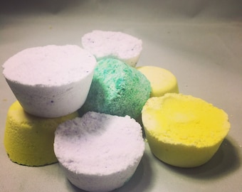 May include: A group of six bath bombs in various colors, including white, green, and yellow. The bath bombs are round and have a slightly textured surface.