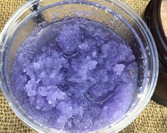 May include: A clear plastic container filled with purple sugar scrub. The scrub has a grainy texture and is wet.