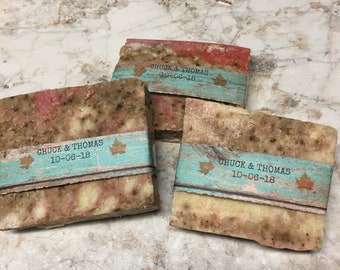 May include: Three bars of handmade soap with a rustic, earthy look. Each bar is wrapped in a turquoise and brown paper label with the text "Chuck & Thomas 10-06-18".
