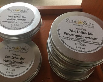 May include: Three silver tins of solid lotion bars, each with a white label. The labels feature the brand name "Sapo de Solis", the product name "Solid Lotion Bar", and the scent "Vanilla Lavender" or "Peppermint Lavender". Each tin is labeled with a price of $10.00 and a weight of 2 oz.