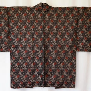 May include: A dark kimono with a repeating paisley pattern in red, black, and beige. The garment is spread out, showcasing the full length and design of the fabric. The kimono has wide sleeves and a collar.