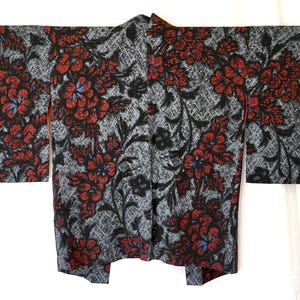 Może przedstawiać: Kimono z kwiatowym wzorem. Ubranie ma szare tło z powtarzającym się wzorem czerwonych kwiatów z niebieskimi akcentami i czarnymi liśćmi. Kimono jest rozłożone, prezentując cały swój wzór.