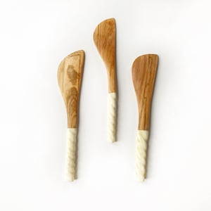 Puede incluir: Tres espátulas de madera con mangos blancos retorcidos. Las espátulas están hechas de madera natural y tienen un color marrón claro.
