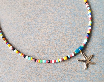 Peut inclure: Un collier de perles colorées avec un pendentif étoile de mer en or. Les perles sont de différentes couleurs, notamment rouge, orange, jaune, vert, bleu et blanc.
