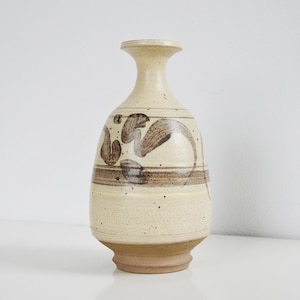 Puede incluir: Un jarrón de cerámica beige con diseños abstractos marrones. El jarrón tiene un cuello estrecho y una base más ancha. Los diseños marrones incluyen líneas curvas y formas orgánicas. El jarrón mide unos 25 cm de altura.